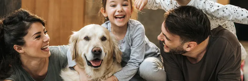 A smiling family of four with a golden retriever dog indoors.